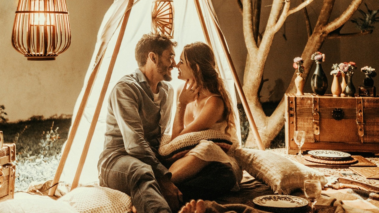 A couple sitting in a makeshift tent in their living room and sharing a tender moment.