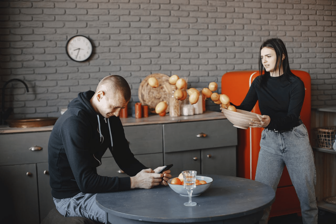 An angry woman throwing fruits at a man using a cellphone.
