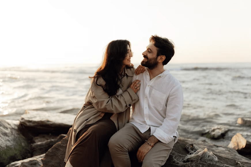 A married couple sitting on a rock at the seaside.