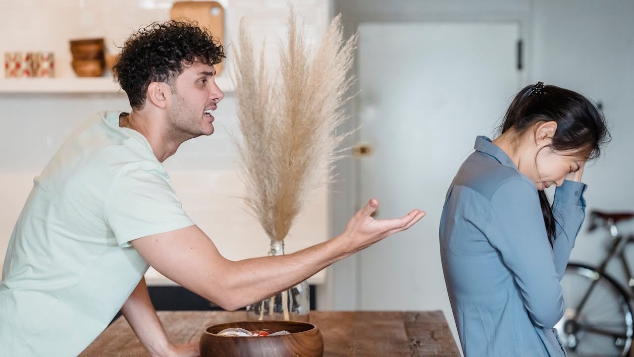 A man is aggressively yelling and gesturing at a woman who is turned away from him