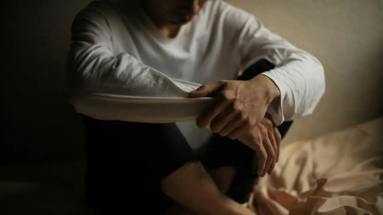 A person in a white long-sleeved shirt sits on the floor with their arms crossed over knees.