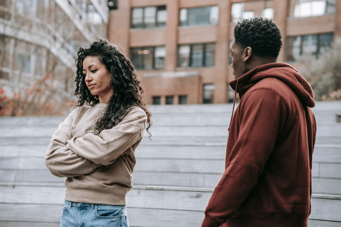 An angry woman turning away from a man as he waits patiently for her to respond.