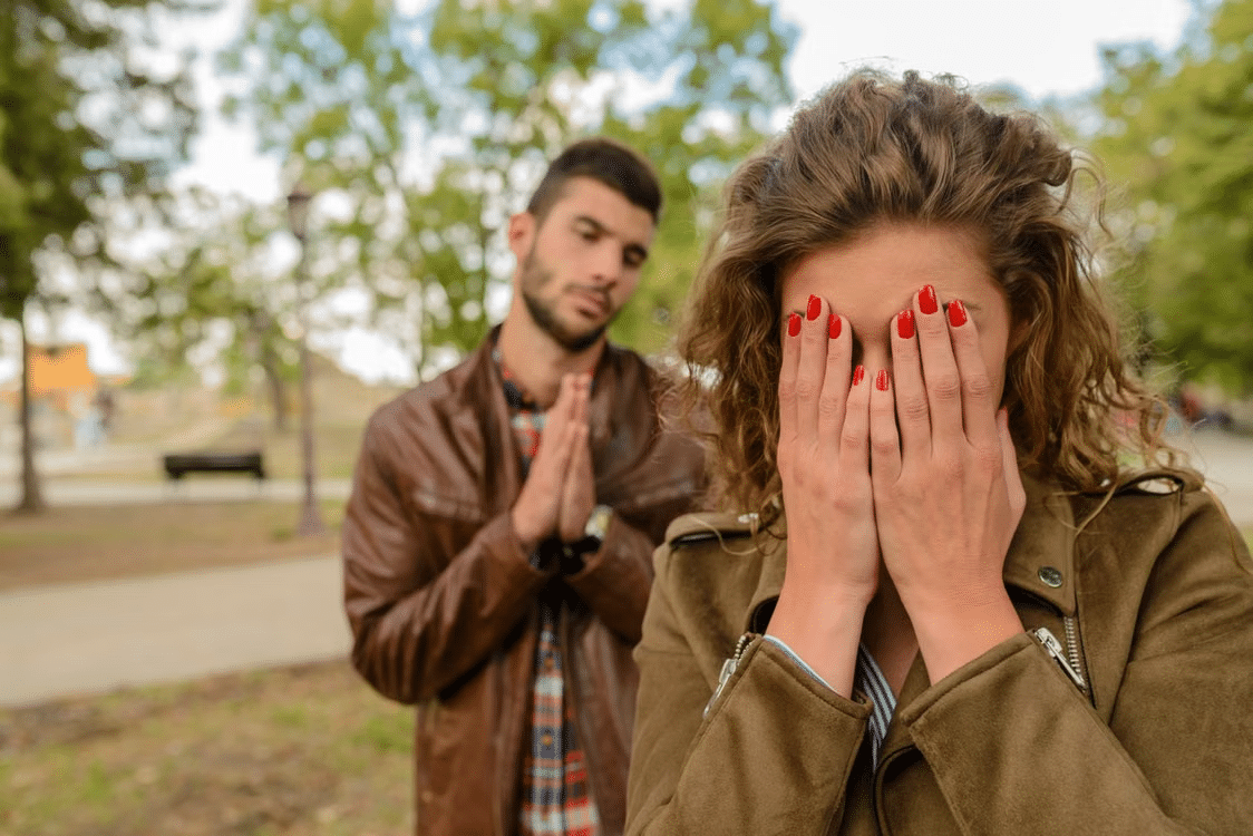 A man folding his hands to say sorry to a woman as she hides her face in her palms.
