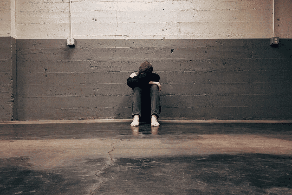A person sitting against a wall crying alone.