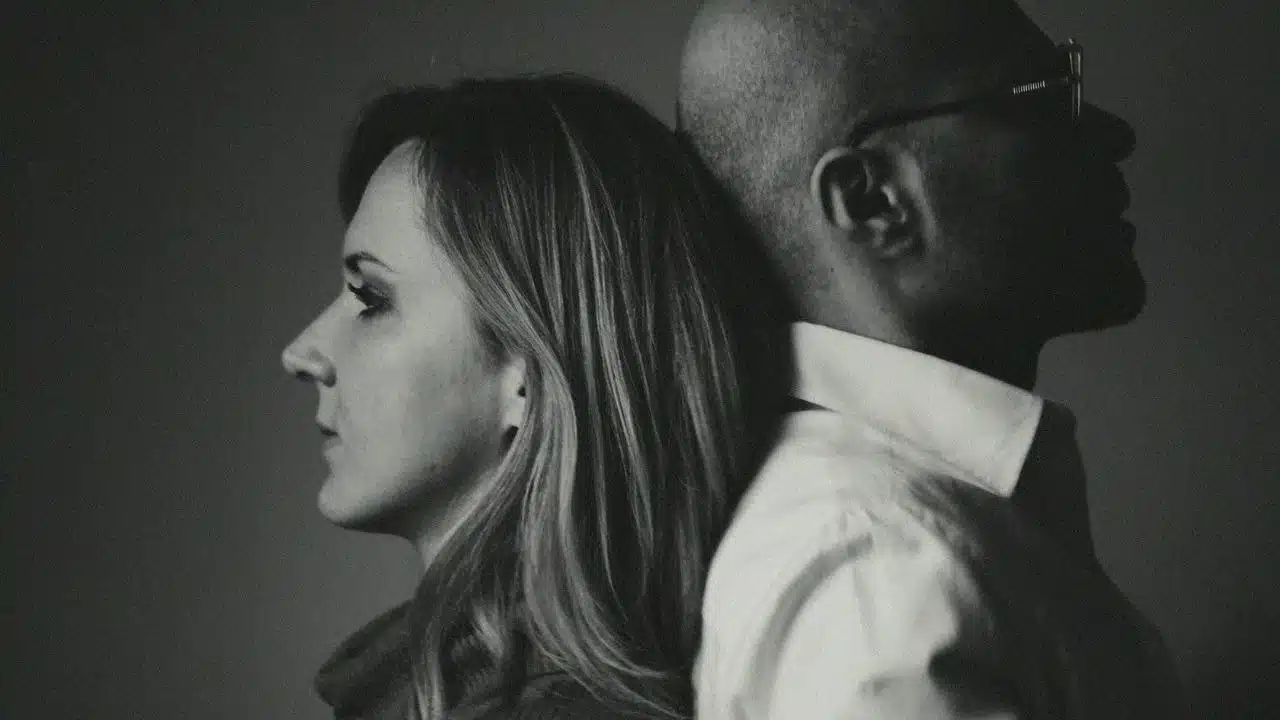 A black and white profile photo of a woman and man leaning back to back.