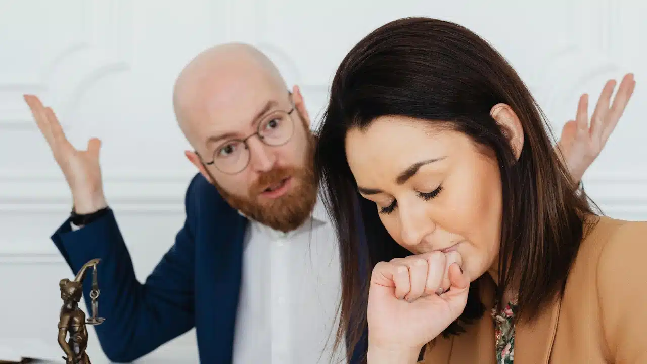A man with glasses making fun of his partner who looks perturbed with closed eyes.