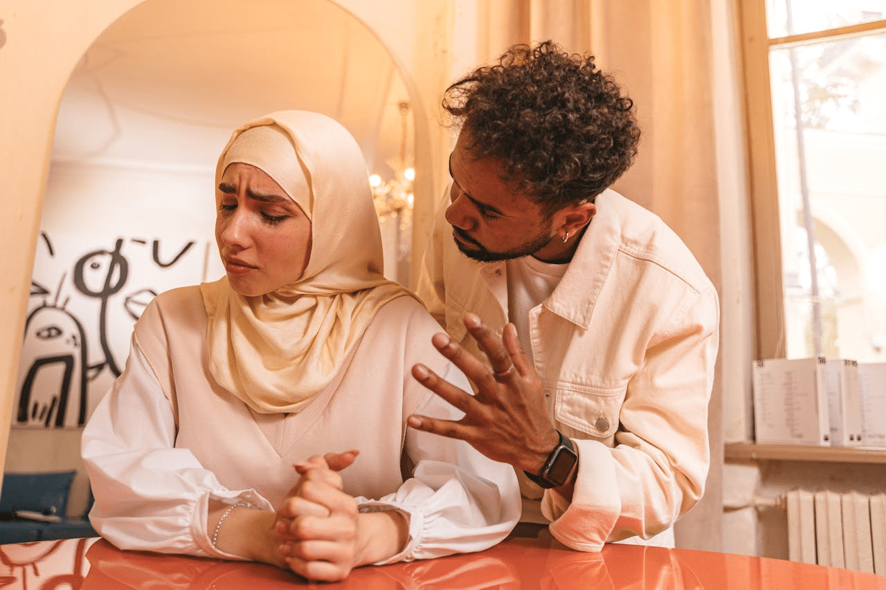 A furious man talking to a man with an unhappy woman in hijab.