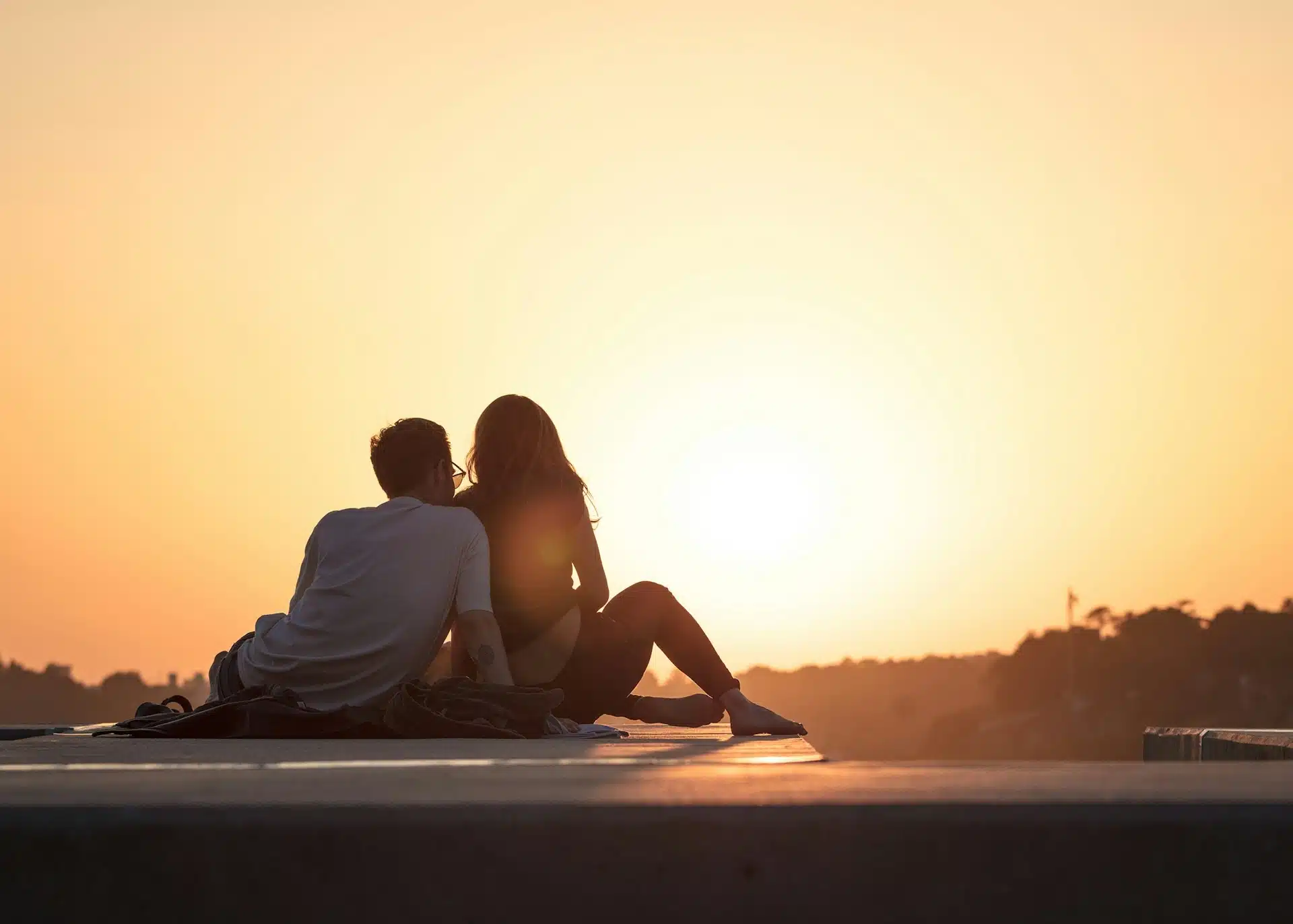 A couple sitting on a ledge watching the sunset together.