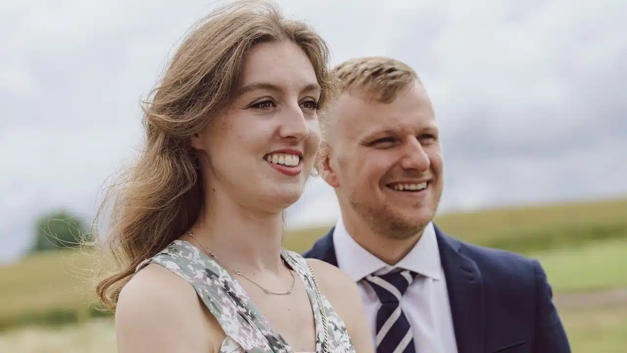 A smiling couple standing next to each other in a field.