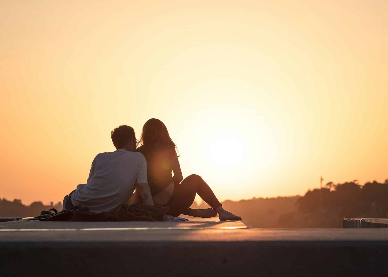 A couple sitting on a ledge watching the sunset together.