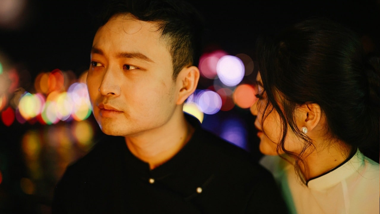 A couple sitting close to each other with colorful lights in the background.