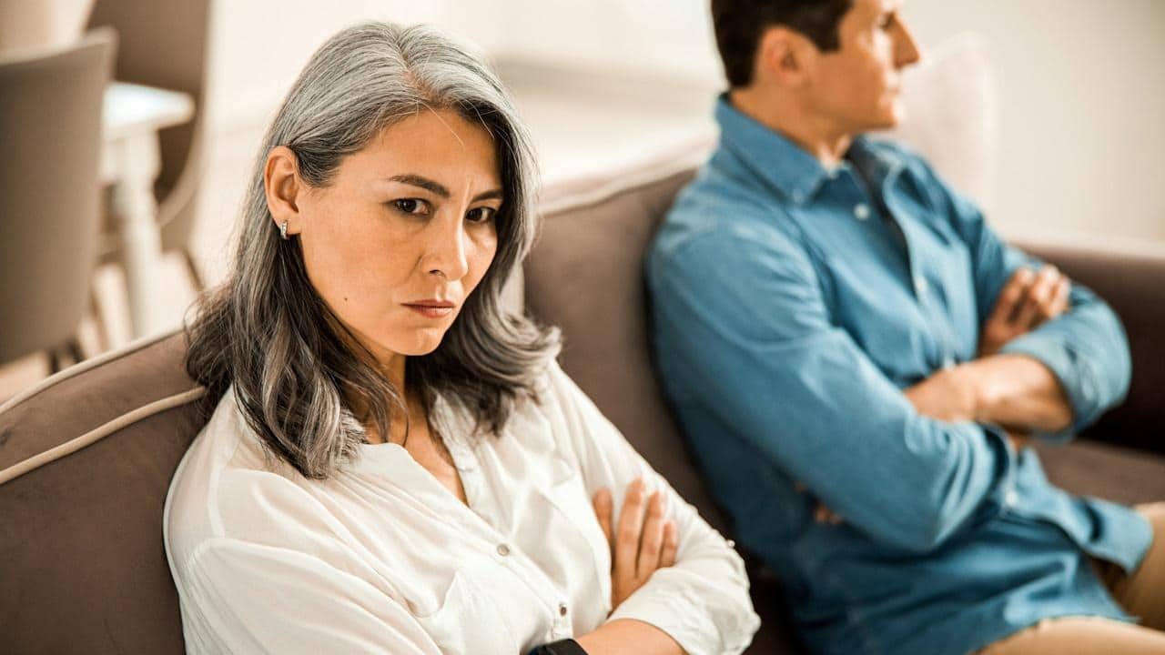 A mature couple is sitting on a couch and refusing to talk to each other.