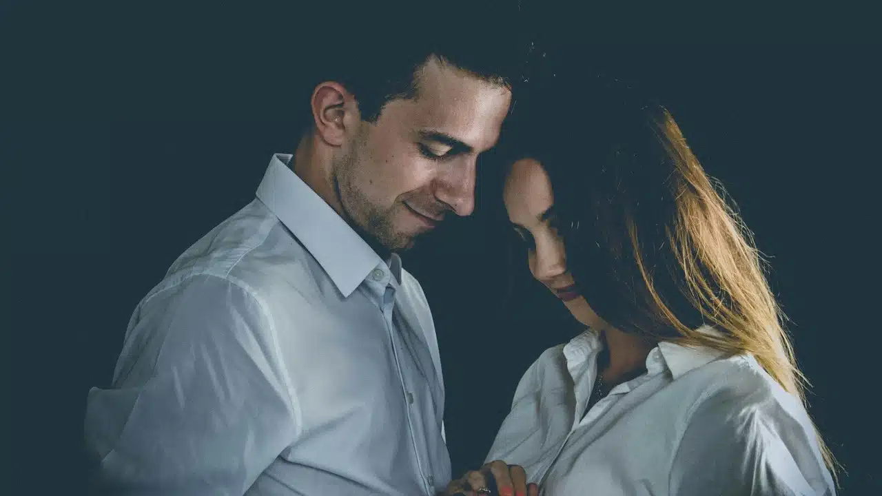 A couple smiling while standing near each other and gazing downwards.