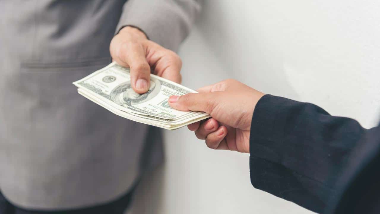 A stack of U.S. dollar bills being passed between two hands.