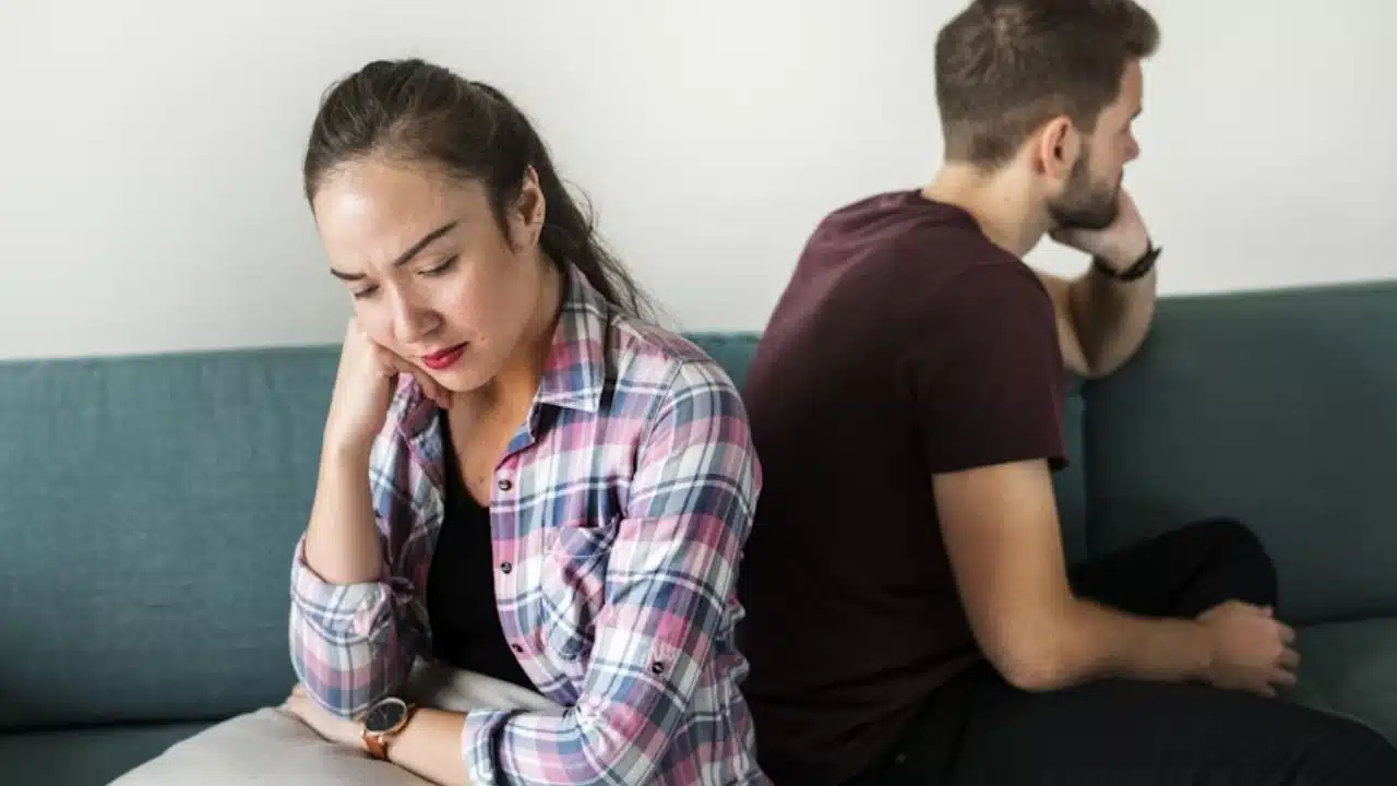 Couple upset with each other sitting back-to-back on a sofa