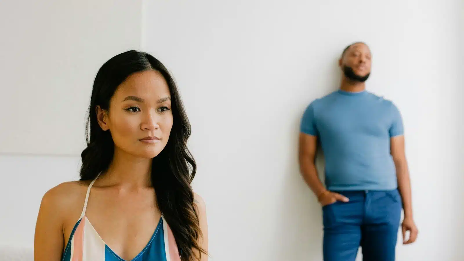 A woman standing with a man leaning against a wall in the background.