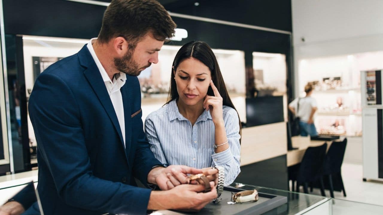 A man in a suit and a woman look closely at watches in a jewelry store.