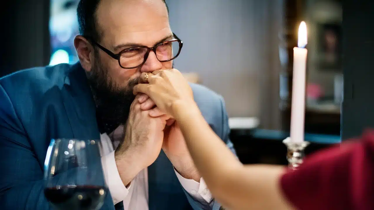 A man in a suit leans forward and kisses a woman's hand at a table.