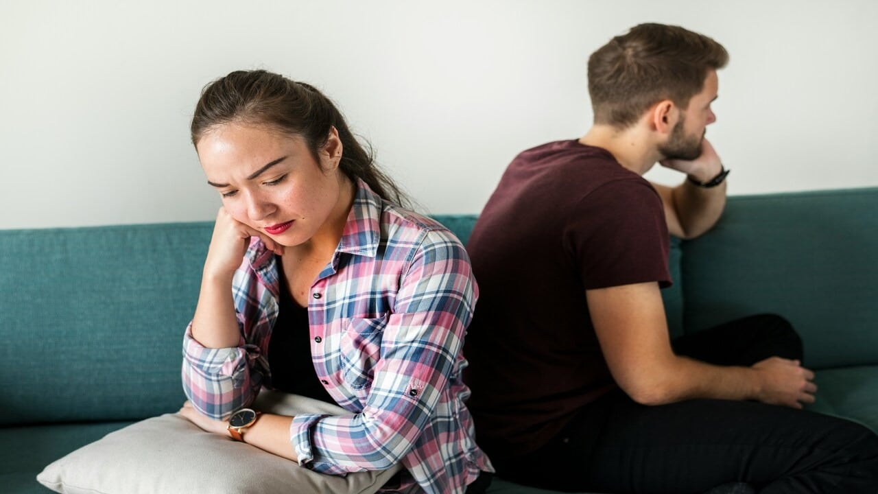 An upset couple sitting on a sofa with their backs against each other.