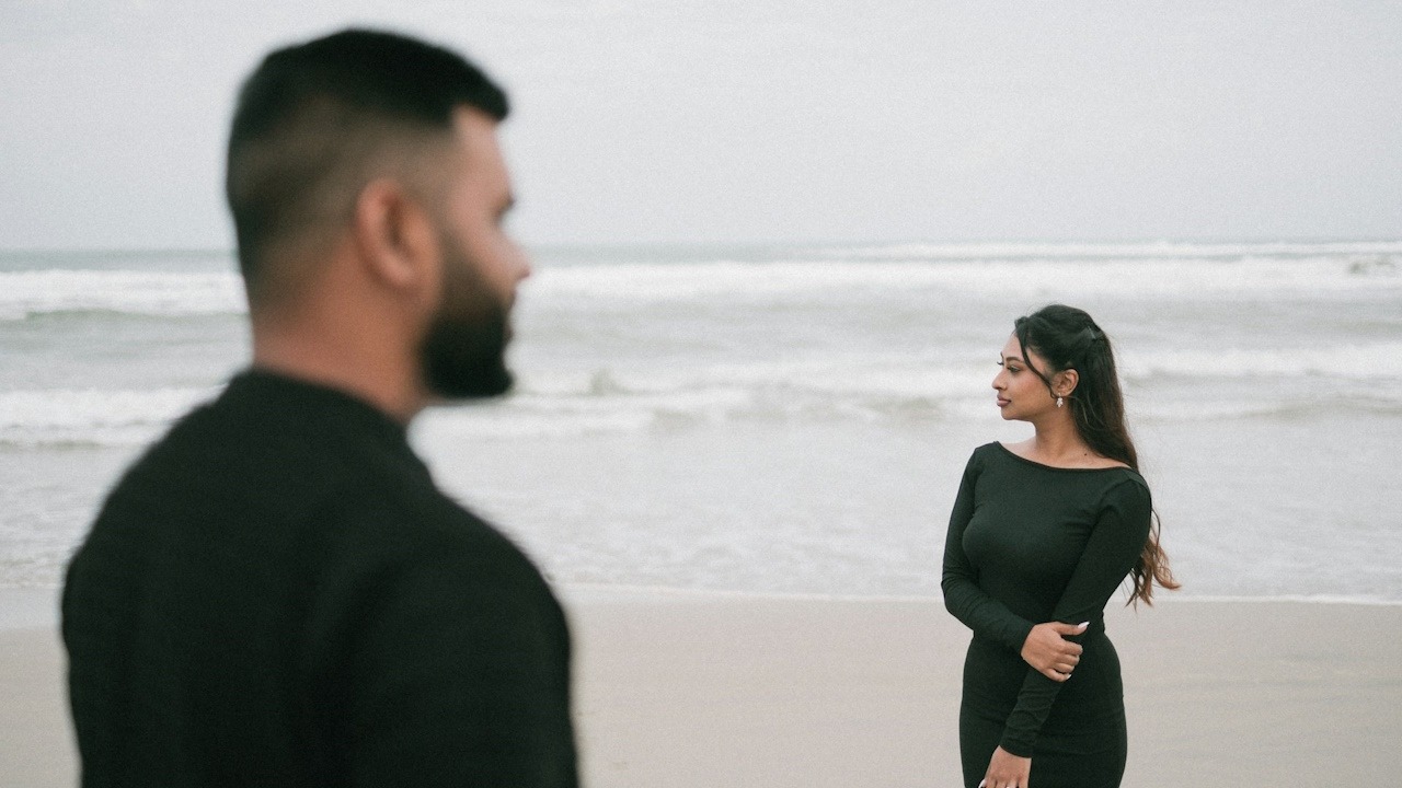 A couple on the beach are facing the ocean.