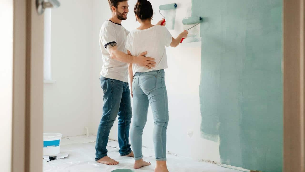 A couple painting a wall together in a bright room.