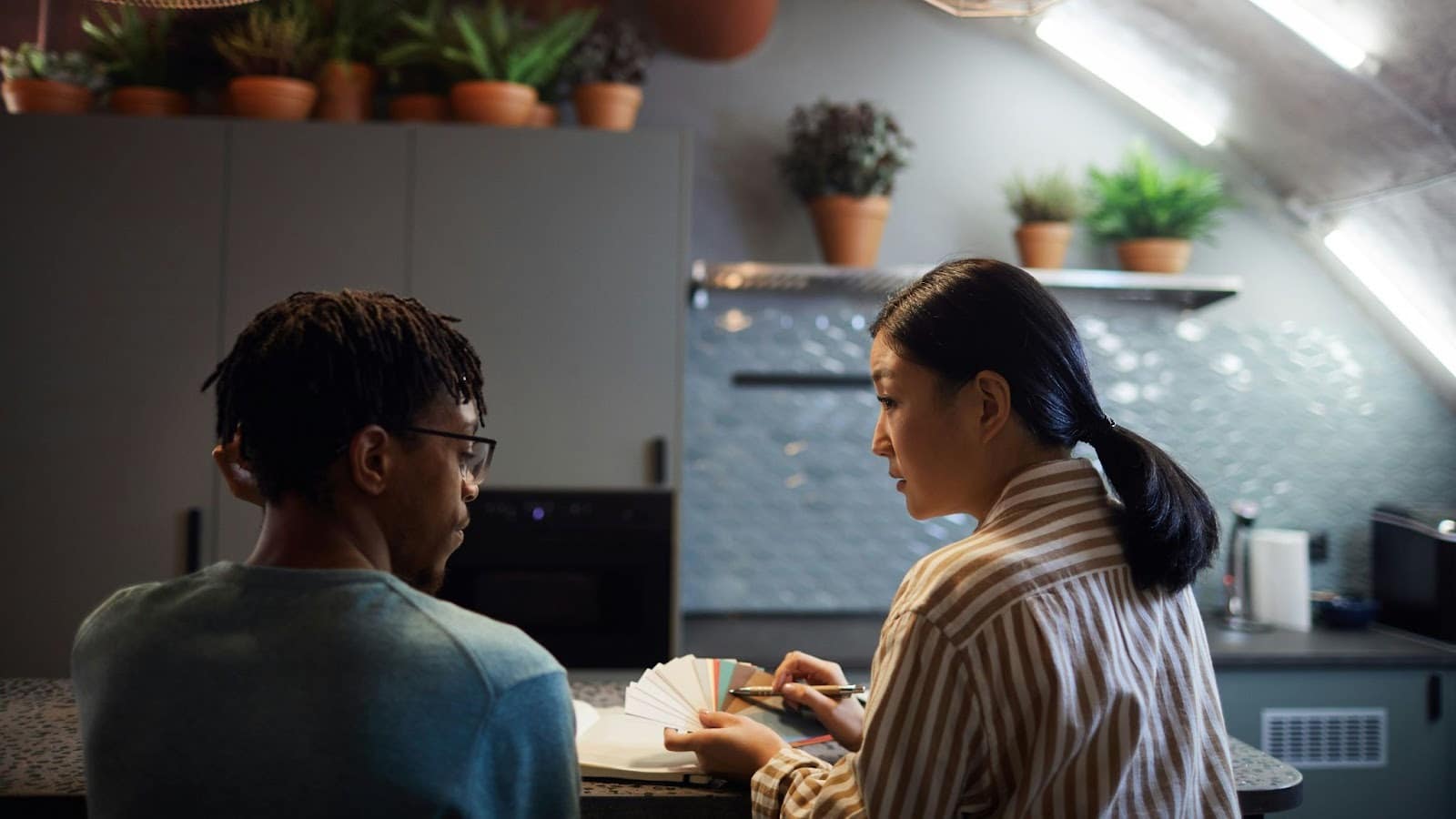 A man and a woman sitting on a kitchen counter discussing something.