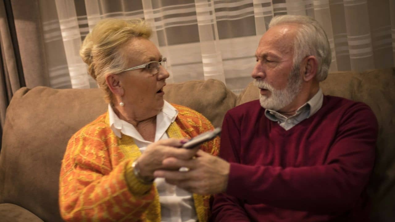 An elderly couple argues playfully while fighting over a remote control.