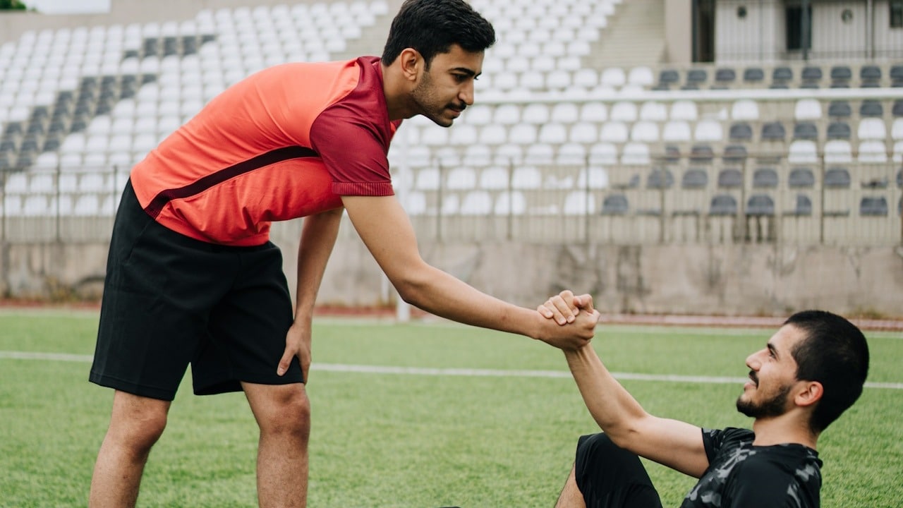 A man is helping another man with a soccer ball.