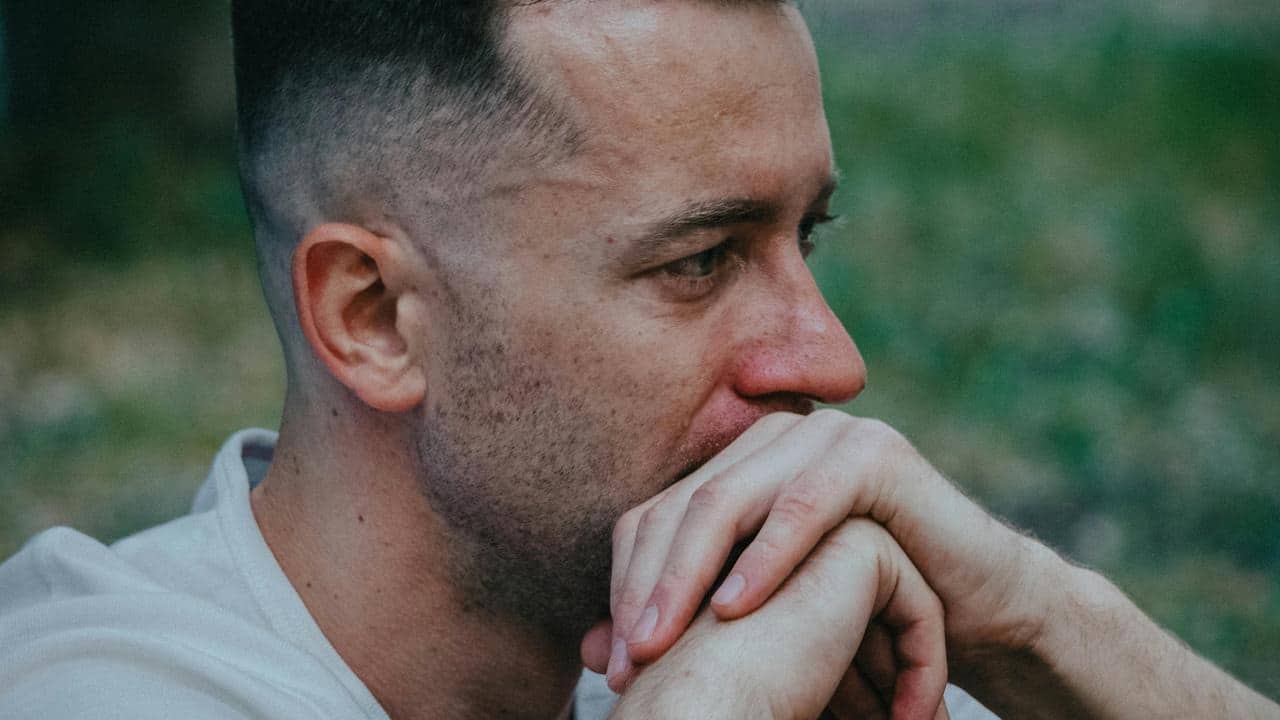 A man resting his hands near his mouth, looking worried and deep in thought.