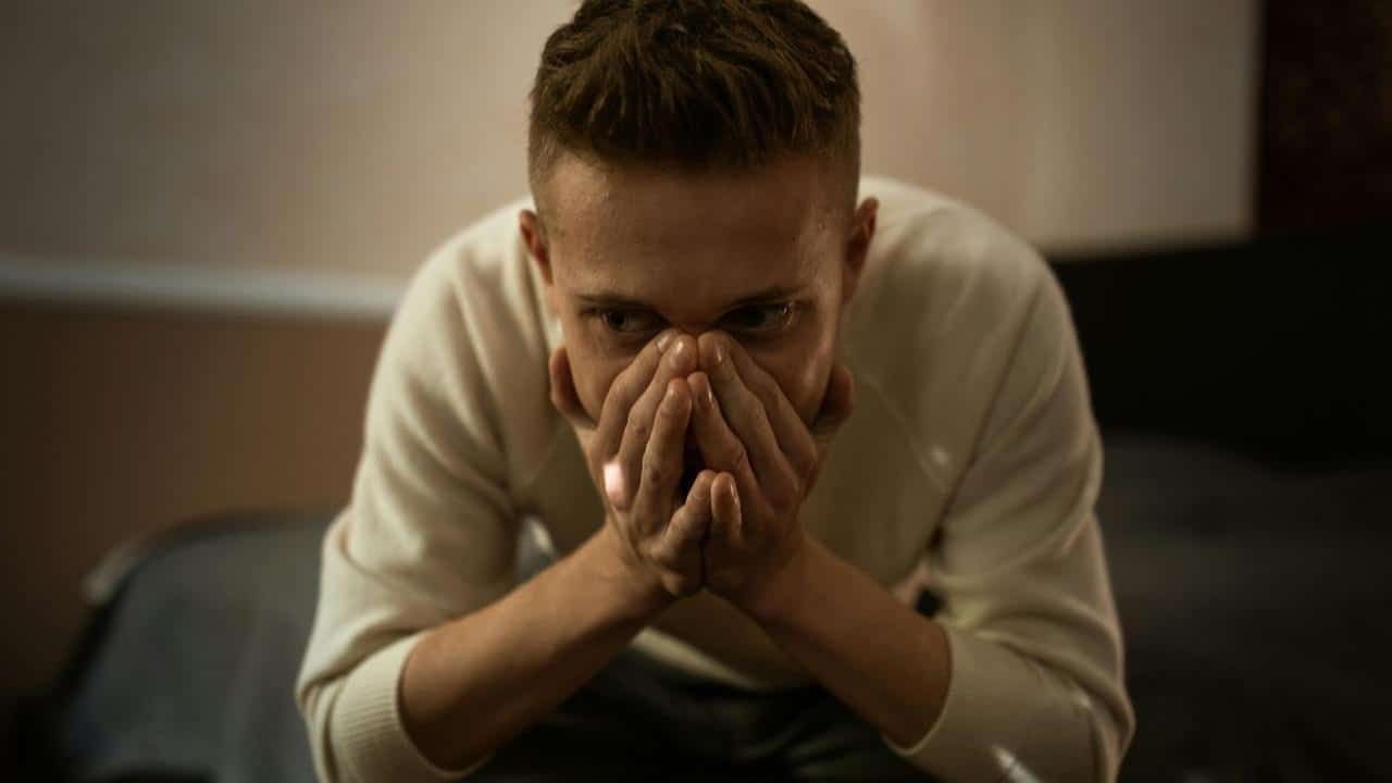 A man leaning forward with his hands covering his mouth, looking anxious.