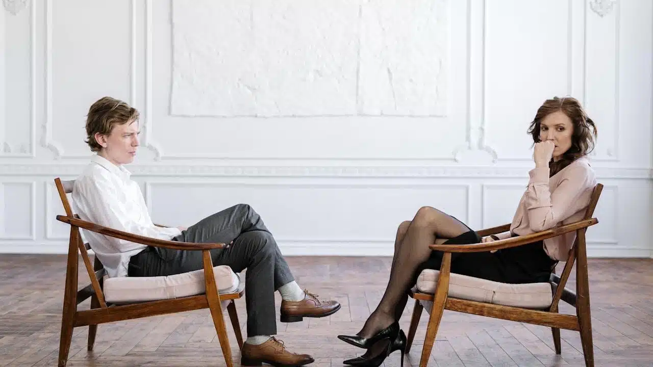 A man and woman sitting on a brown wooden chair.