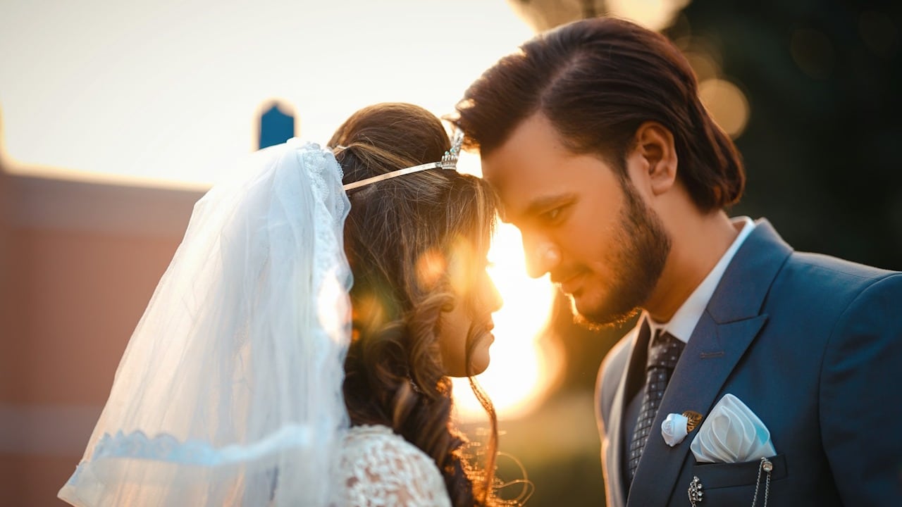 Bride and groom touching foreheads outdoors with backlighting, focused on their faces.
