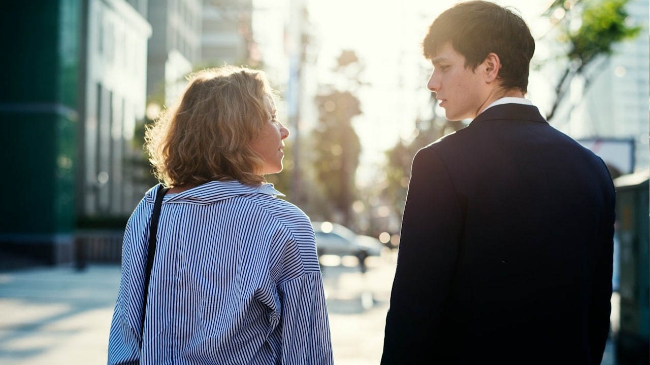 Woman in a striped shirt looking back at a man in a dark suit walking on a sunny city street