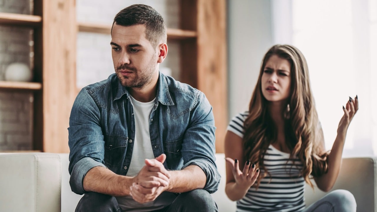 Man looking away sadly while woman argues in background.