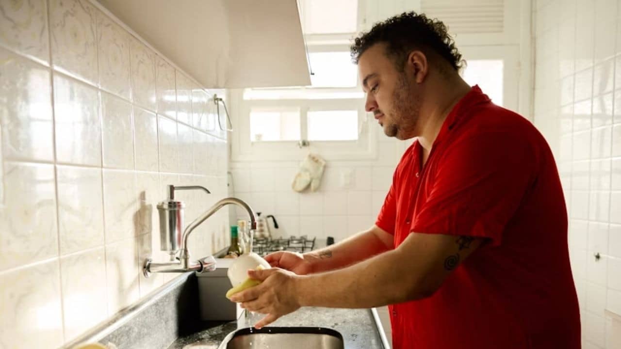 Man in casual clothes at kitchen sink washing dishes