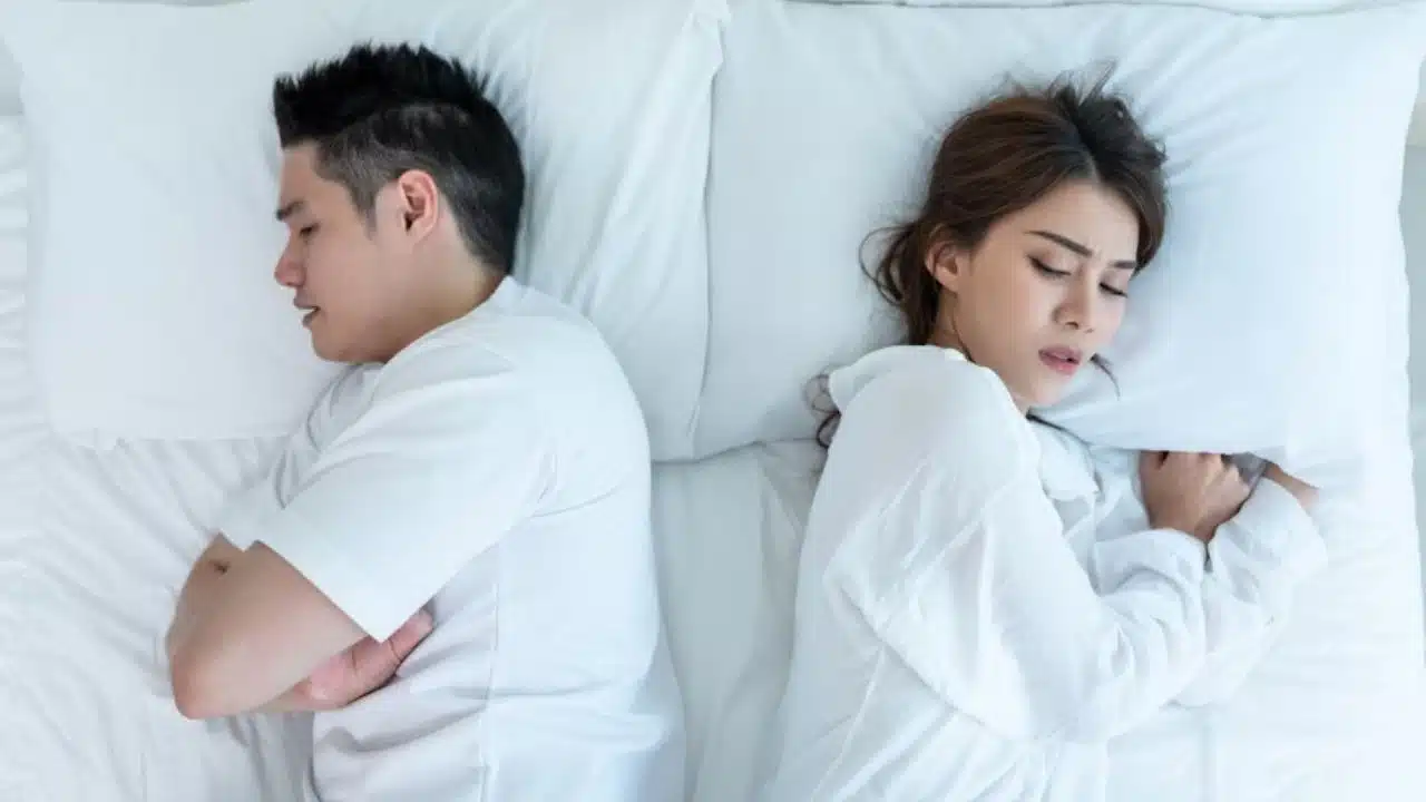 Couple lying in bed back to back looking distant