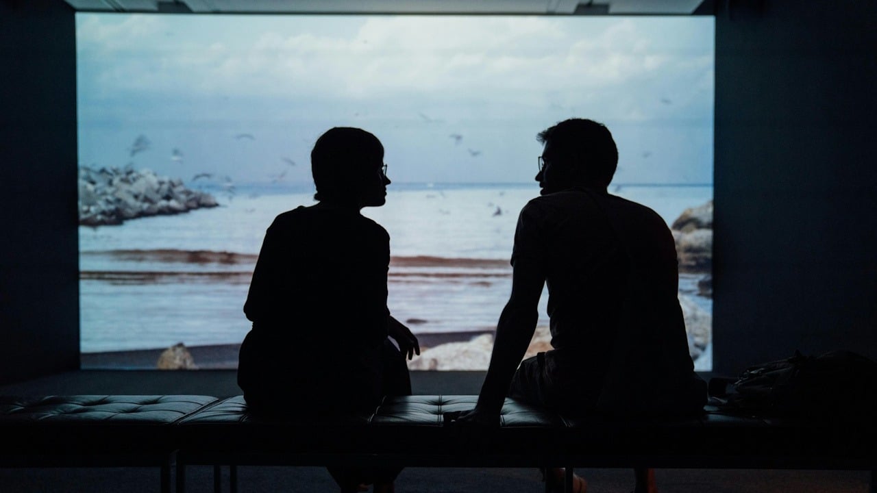 The dark silhouettes of a couple sit on a bench, facing each other in conversation.