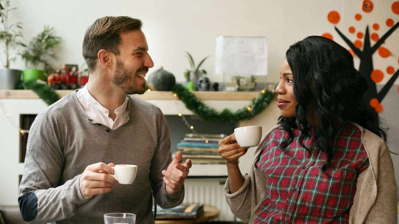 A couple having coffee at a cafe with the woman smiling and listening to the man.