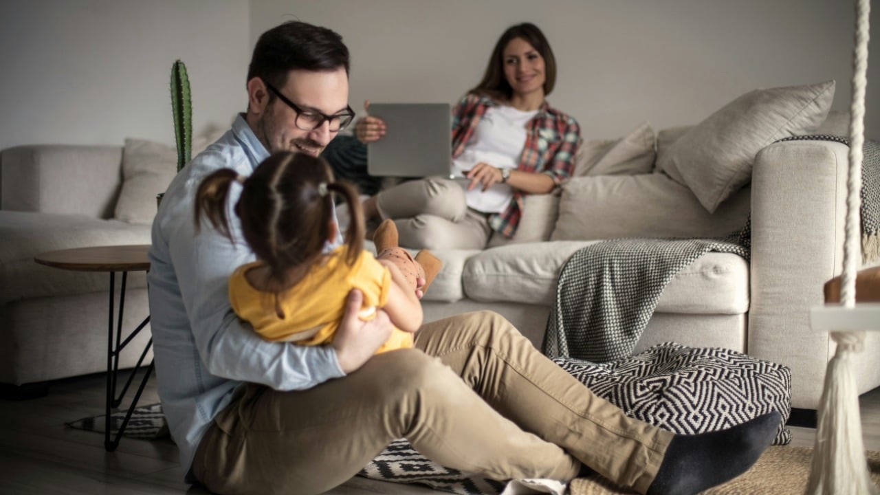 A man sits on the floor holding a small child while a woman watches.