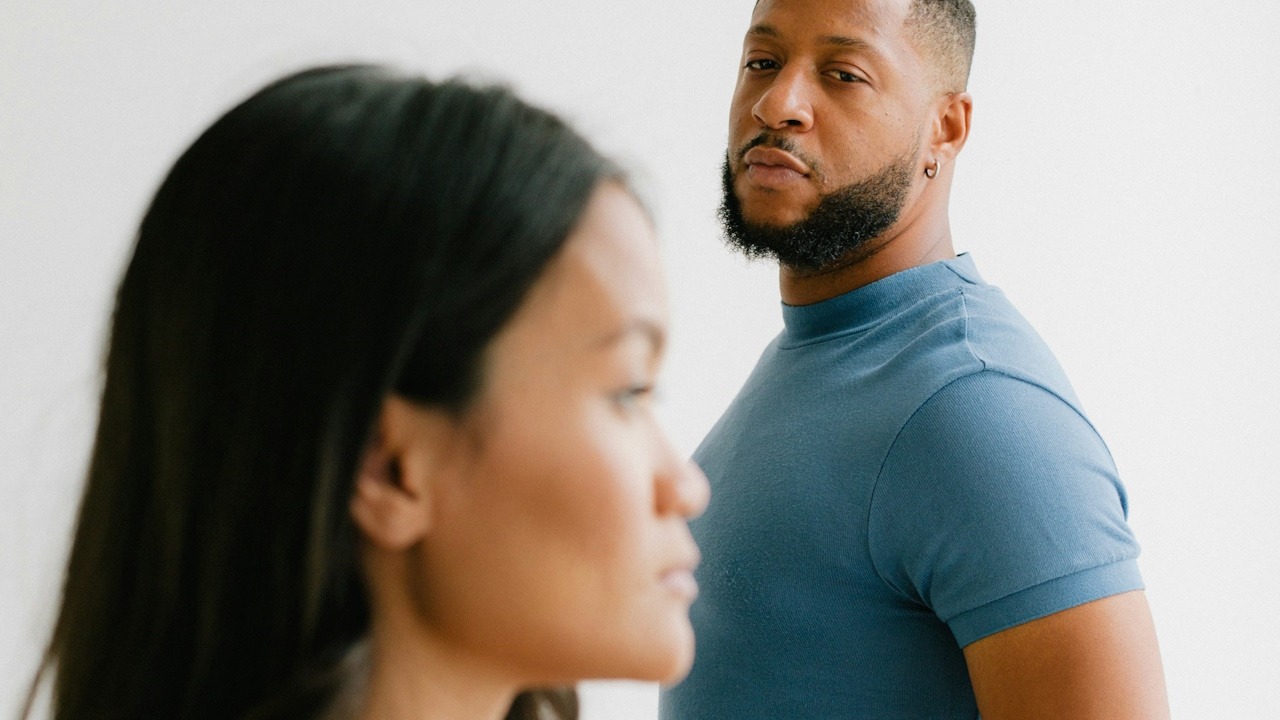 A bearded man looking at a woman who stares straight ahead.