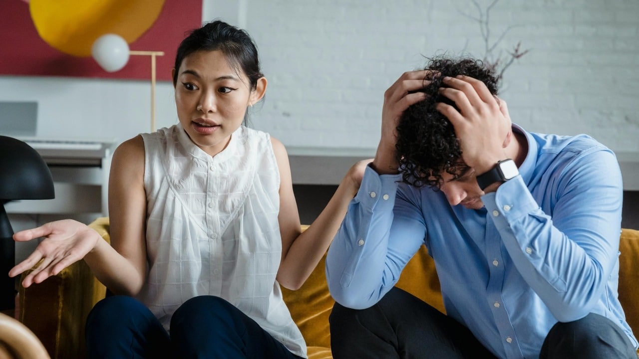 A woman gestures while speaking to a man who has his hands on his head in distress.