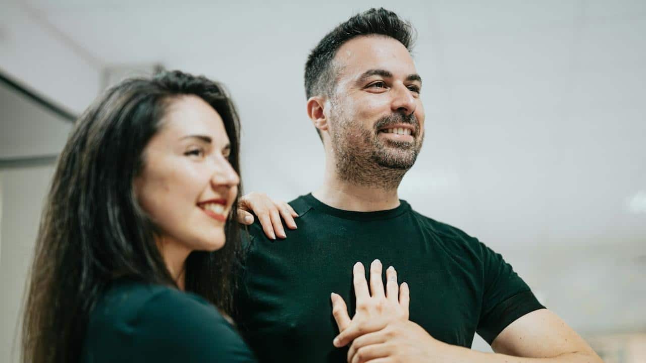 A man standing next to a woman in a room who has her hand placed on his chest.