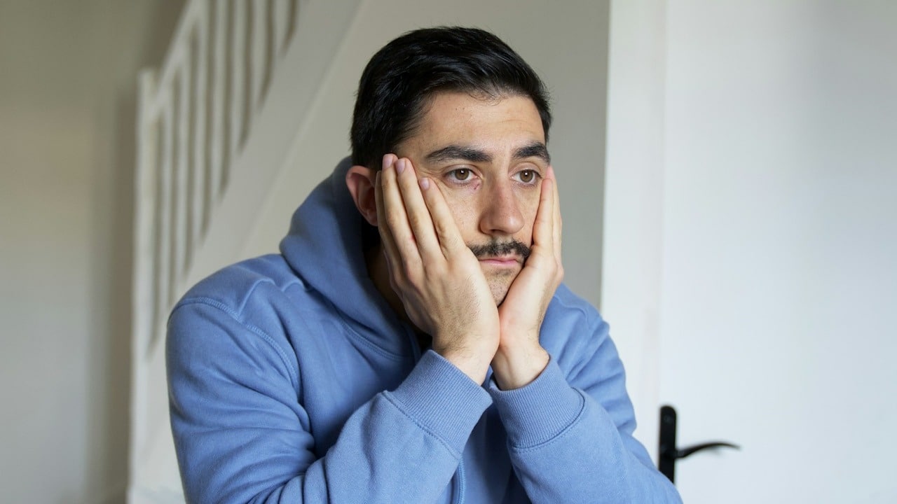 A person sitting at a desk with the hands on the face.