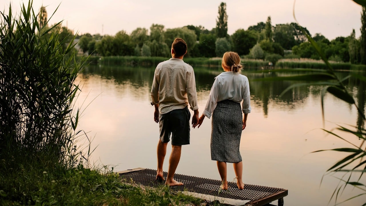 A couple standing on a deck over a lake and holding hands.
