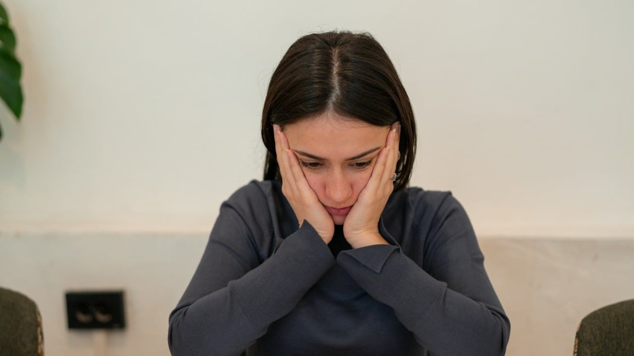 A sad woman is sitting with her face in her hands.