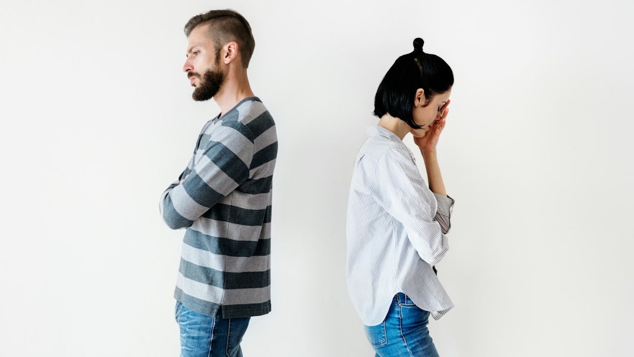 An upset couple standing with their backs against each other.