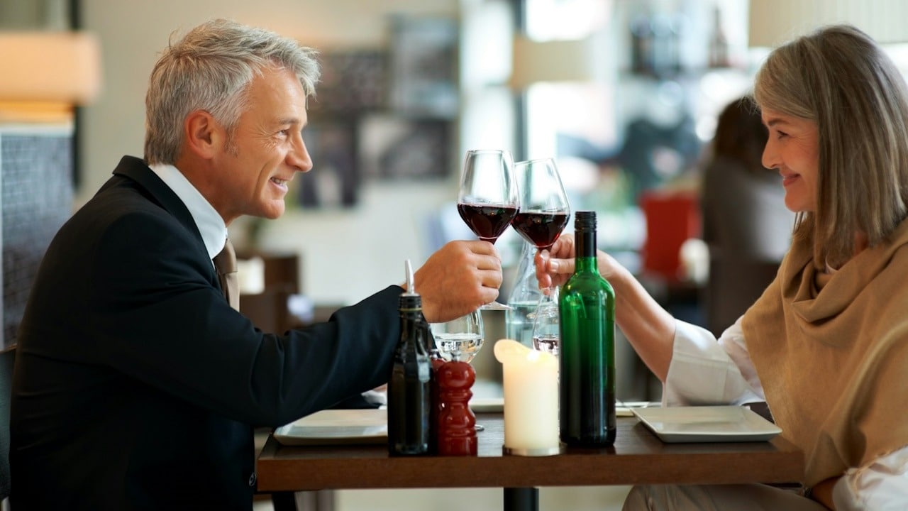 A mature couple on a date clinking glasses and making a toast while sitting at a table.