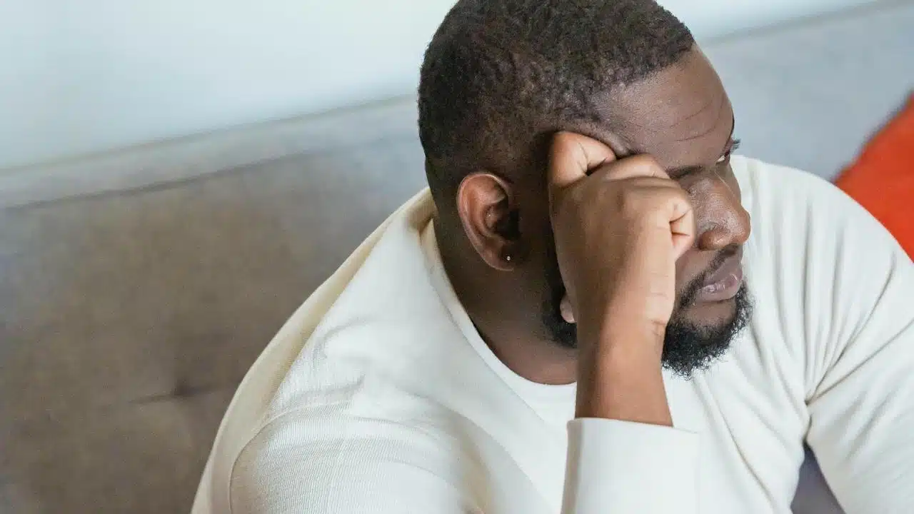 A man in a white shirt resting his head on his hand with a worried expression.