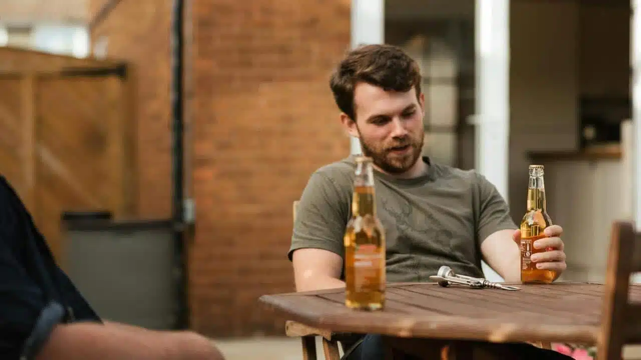 A man sitting at a table holding a beer bottle with another bottle in front of him.