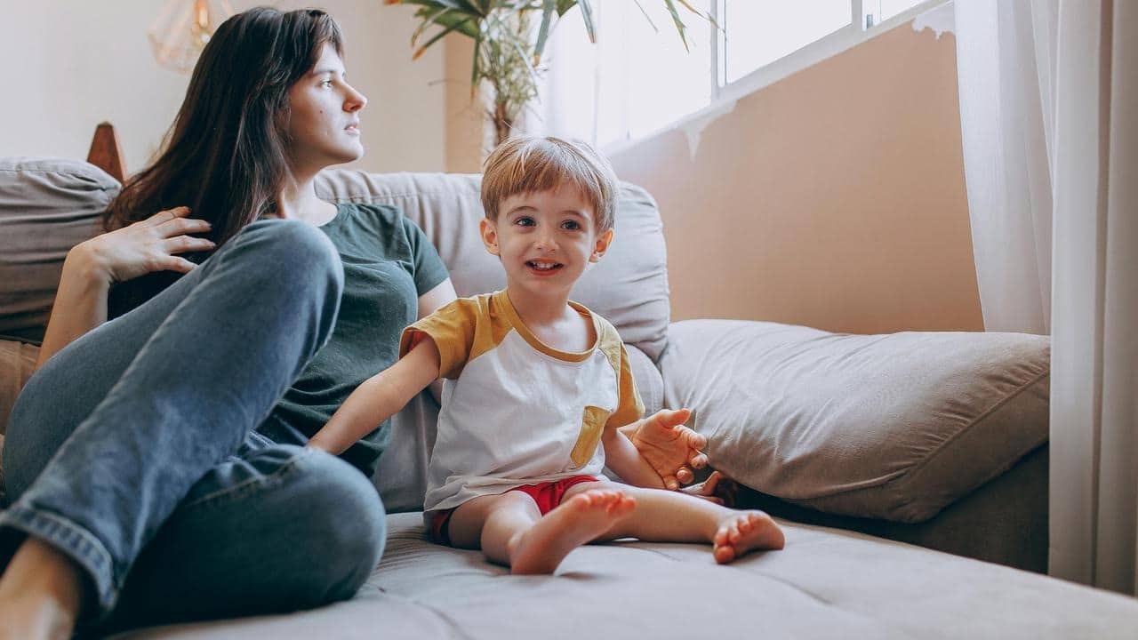 A woman sitting on a couch beside a smiling young boy.